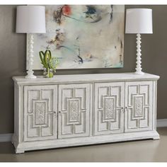 a white sideboard with two lamps and a painting on the wall in the background