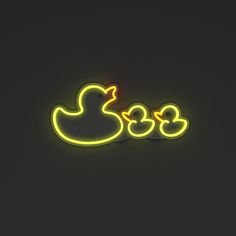 two neon ducks sitting next to each other on a black surface with the light turned on