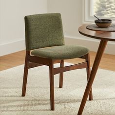 a wooden table with a bowl on top of it next to a chair that has a green upholstered seat