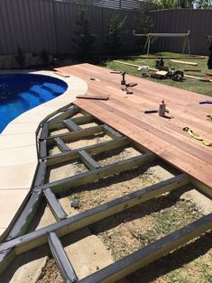 a wooden deck next to a swimming pool with tools laid out on the ground around it