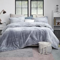 a bedroom with grey bedding and two windows