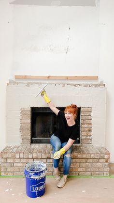 a woman in black shirt and yellow gloves painting a brick fireplace