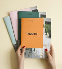 a person holding an orange book in front of four different colored books on a table