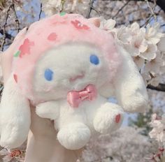 a white stuffed animal wearing a pink bow tie with cherry blossoms in the back ground