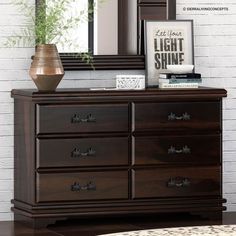 a brown dresser sitting next to a mirror on top of a wooden floor with a plant in front of it