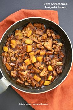 a skillet filled with meat and potatoes on top of a red cloth next to a knife