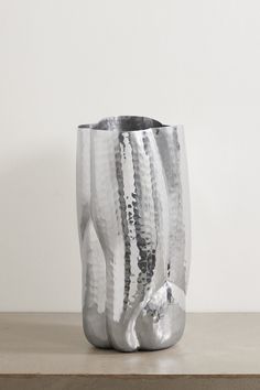 a large silver vase sitting on top of a wooden table next to a white wall