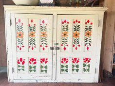 an old white cabinet with painted flowers on the front and side doors, sitting in a room