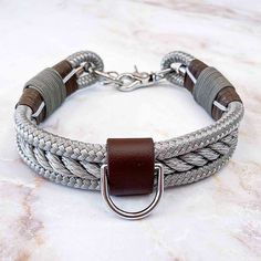 a gray and white braided leather bracelet with a metal clasp on a marble surface