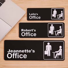 three black and white office signs on a wooden table next to a laptop computer,