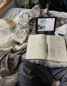 a dog laying on top of a bed next to an open book and tablet computer