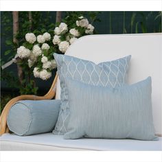 two blue pillows sitting on top of a white couch next to a vase with flowers