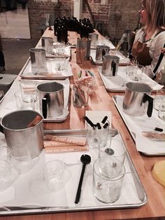 a wooden table topped with metal pans filled with glasses and utensils on top of it