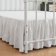 a white bed with ruffled bedspread and wooden floors in front of it