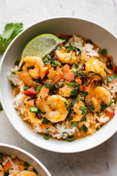 two bowls filled with shrimp and rice on top of a white table next to cilantro