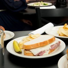 two white plates with sandwiches and chips on them sitting on a table next to a glass of water