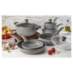 an assortment of grey pots and pans on a white counter top with tomatoes in the background