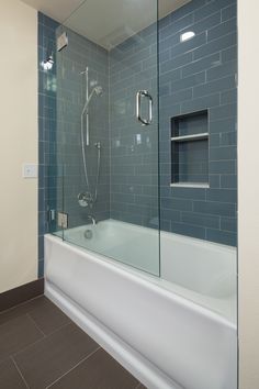 a bath tub sitting next to a shower in a bathroom with blue tile on the walls