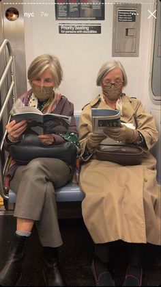 two older women sitting on a train with masks over their faces, reading books and looking at the camera