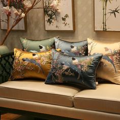 a couch with many pillows on it in front of some pictures and flowers hanging on the wall