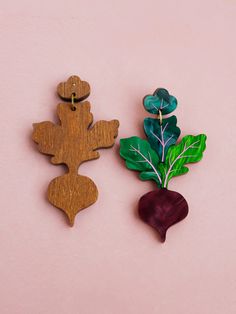 two wooden broccoli and leaf decorations on a pink background