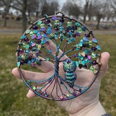 a hand holding a tree of life brooch with an owl on it's back