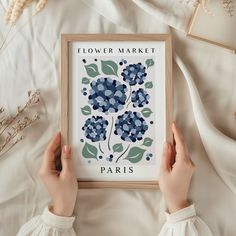 a person is holding up a framed poster with blue flowers on it and the words flower market paris