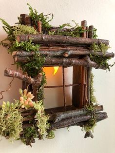 a small wooden birdhouse with moss growing on it's sides and a lit candle in the window