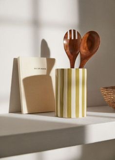 two wooden spoons in a striped cup next to a notepad and book on a shelf