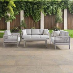 an outdoor patio with white furniture and greenery on the fenced in wall behind it