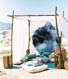 an outdoor seating area on the beach with blue and white pillows, blankets and other items