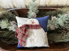 a snowman pillow sitting on top of a wooden tray next to pine cones and evergreen branches