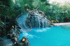 an outdoor swimming pool with waterfall and rocks