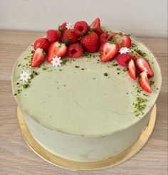 a white cake with strawberries and daisies on top, sitting on a wooden table