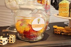 there is a glass jar filled with gummy bears and dices on the table