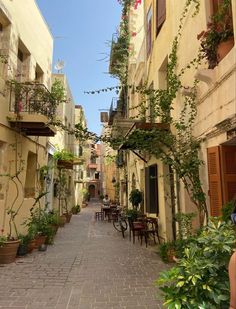 an alley way with tables and chairs lined up along the side walk, surrounded by potted plants