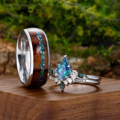 two wedding rings with opal and diamond accents on top of a wooden table in front of some trees