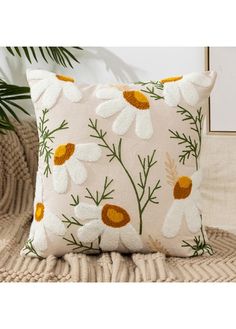 a pillow with daisies on it sitting on a couch next to a potted plant