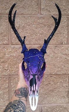 a hand holding up a purple and black animal skull with horns on it's head