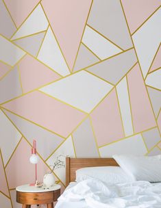 a white bed sitting under a pink wall next to a wooden table with a lamp on it