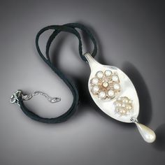 a silver spoon with pearls on it sitting next to a black cord and a white bead necklace