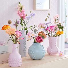 three vases filled with different types of flowers on a table next to a window