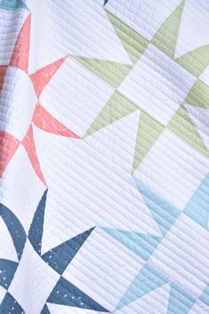 a close up of a quilt on a bed with an orange, white and blue star design