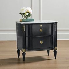 a black cabinet with marble top and gold trimmings on the bottom, along with a flower in a vase