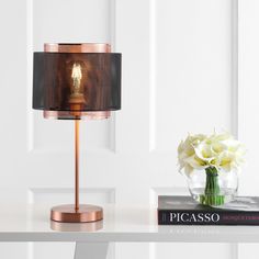 a lamp on a table next to a book and vase with white flowers in it