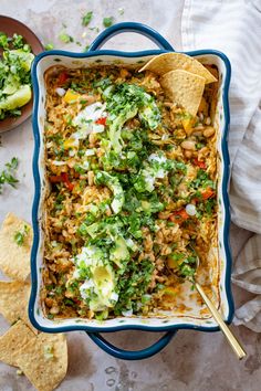 a casserole dish filled with mexican food and tortilla chips on the side