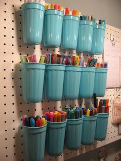 there are many cups on the wall with markers and pencils in them as well