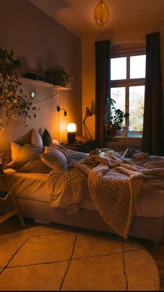 a bedroom with a bed, lamp and plants on the windowsills at night