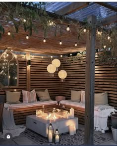 an outdoor seating area with candles and lights on the ceiling, surrounded by wood slats