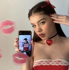 a woman holding up her cell phone to take a selfie with lips drawn on the wall behind her